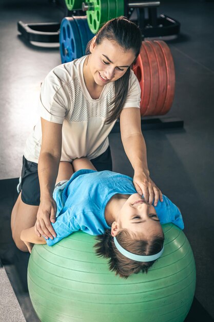 Una niña linda estirándose en una pelota de pilates con su madre en el gimnasio.