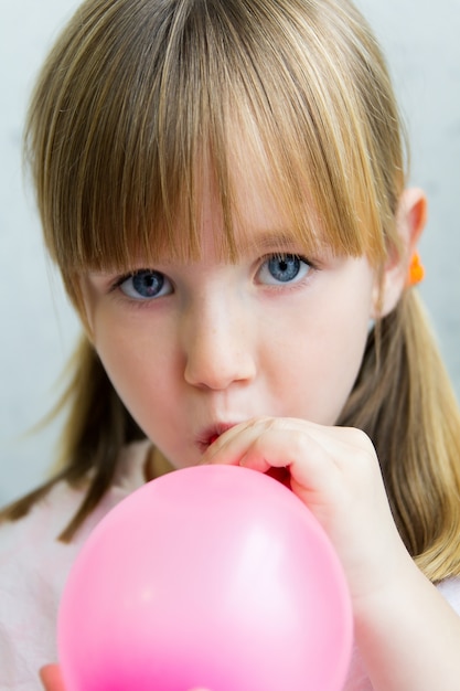 Niña linda inflar un globo de color rosa en la cocina