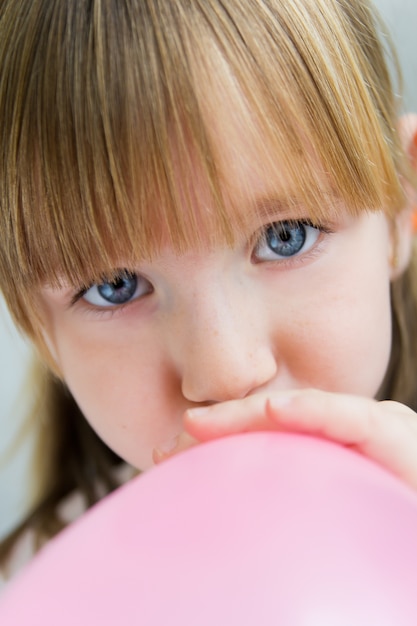 Niña linda inflar un globo de color rosa en la cocina