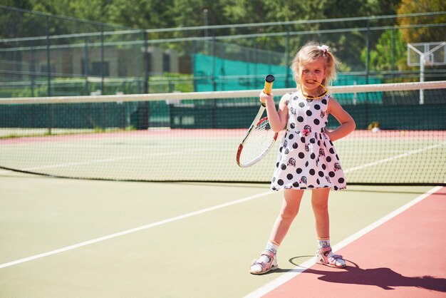 Niña linda jugando al tenis en la cancha de tenis afuera.