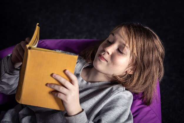 Una niña linda lee un libro acostado en un puf