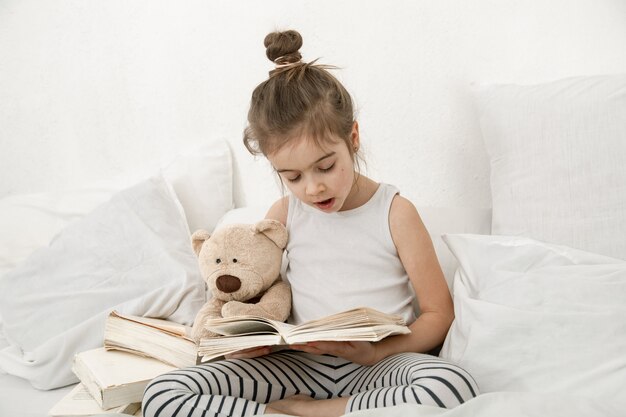 Niña linda leyendo un libro en la cama en el dormitorio.