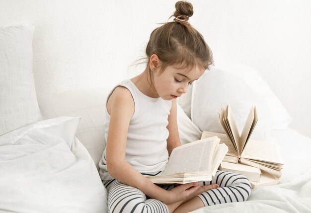 Niña linda leyendo un libro en la cama en el dormitorio.