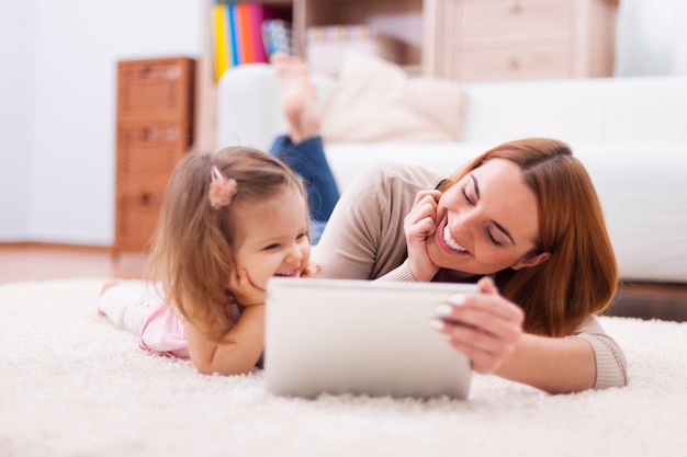 Niña linda con mamá con tableta digital en casa