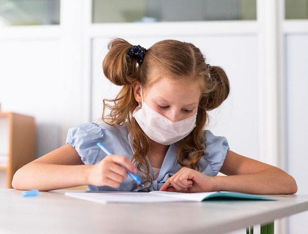 Niña linda con una máscara médica mientras escribe