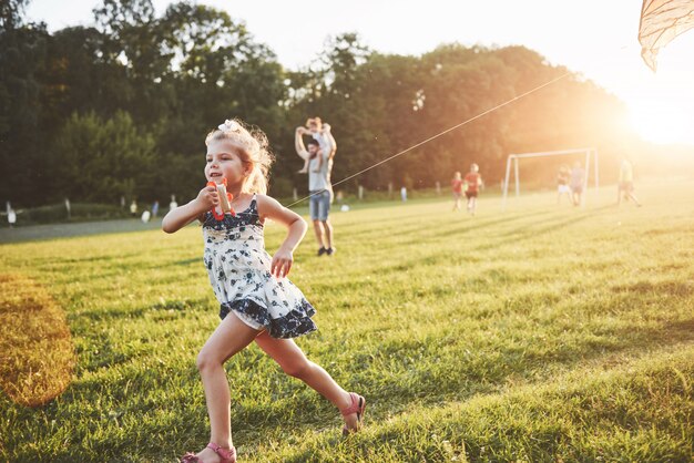 Niña linda con el pelo largo con cometa en el campo en un día soleado de verano