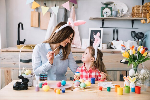Niña linda pintando huevos para pascua con madre