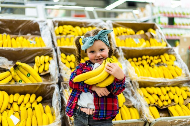 Niña linda con plátanos en una tienda de alimentos o supermercado