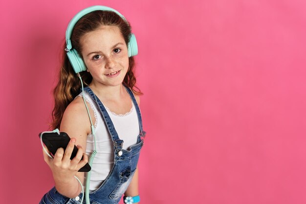 Niña linda posando con un teléfono y auriculares sobre un fondo rosa