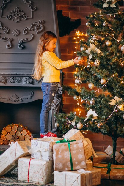 Niña linda que adorna el árbol de navidad