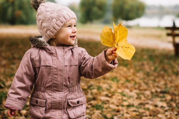La niña linda que ase hojas amarillas en parque del otoño