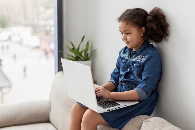 Niña linda que hojea la computadora portátil en casa