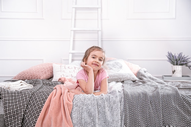 Niña linda que juega en la cama. Mira pensativamente y descansa.