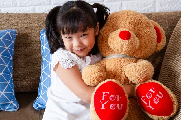 Niña linda que muestra gran oso de peluche con felicidad