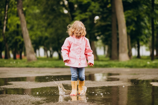 Niña linda saltando en el charco en un clima lluvioso