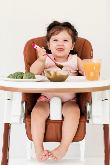 Niña linda sentada en su mesa delante de brócoli y jugo