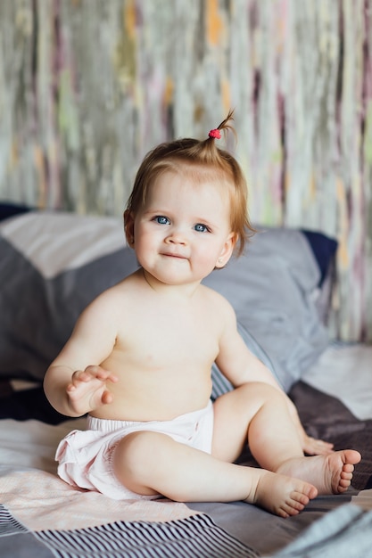 Niña linda se sienta en la cama con un bonito peinado en el dormitorio