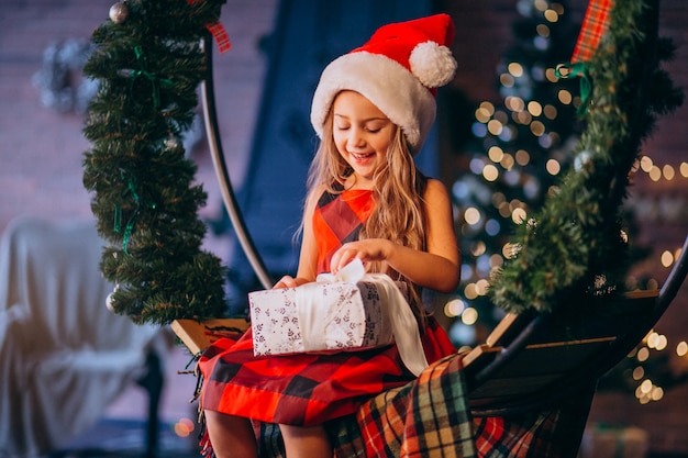 Niña linda en el sombrero de santa que desempaqueta el regalo de Navidad