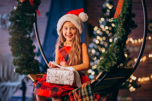 Niña linda en el sombrero de santa que desempaqueta el regalo de Navidad