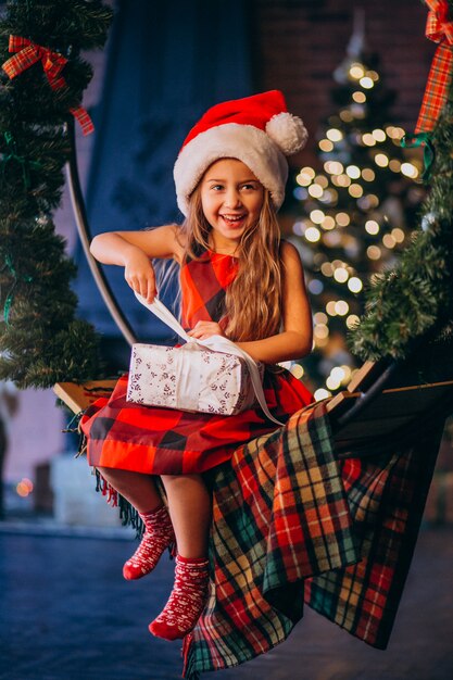 Niña linda en el sombrero de santa que desempaqueta el regalo de Navidad