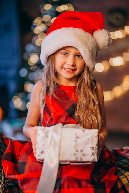 Niña linda en el sombrero de santa que desempaqueta el regalo de Navidad