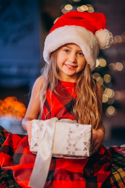 Niña linda en el sombrero de santa que desempaqueta el regalo de Navidad