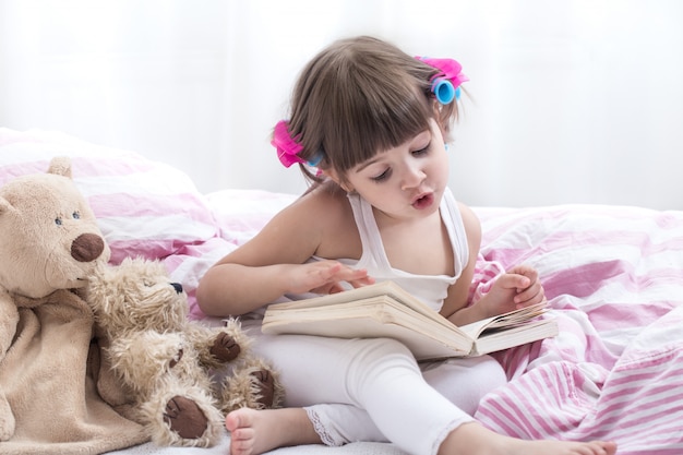 Niña linda sonriendo mientras está acostado en una acogedora cama blanca