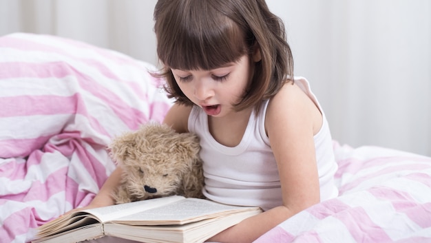 Niña linda sonriendo mientras está acostado en una acogedora cama blanca