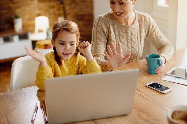 Una niña linda y su madre tienen una videollamada en una computadora portátil en casa