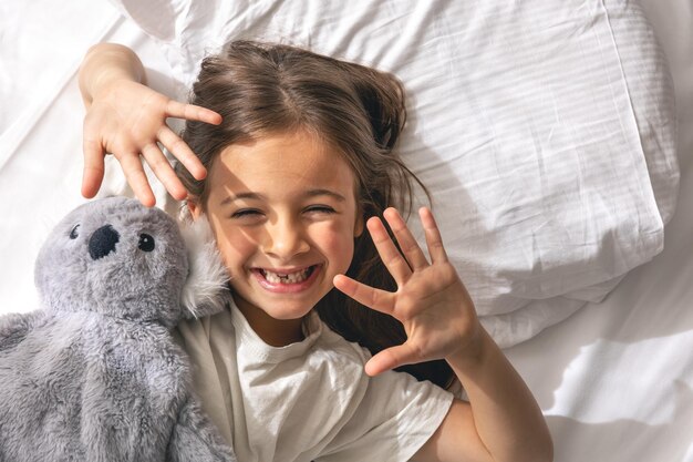 Niña linda con su peluche favorito en la cama por la mañana