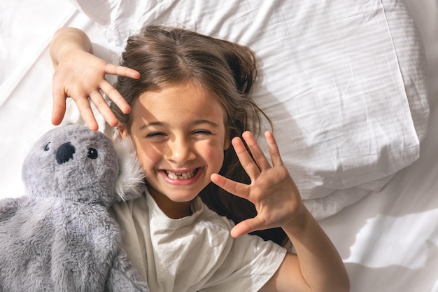 Niña linda con su peluche favorito en la cama por la mañana