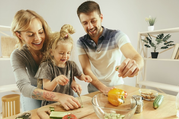 Niña linda y sus hermosos padres están cortando verduras