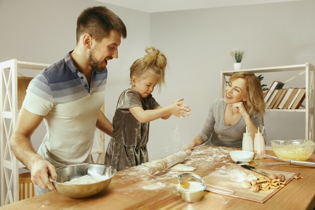 Niña linda y sus hermosos padres preparando la masa para el pastel en la cocina de casa. Concepto de estilo de vida familiar