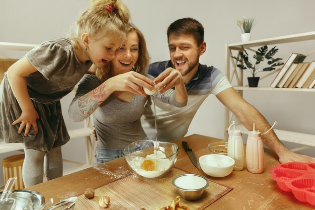 Niña linda y sus hermosos padres preparando la masa para el pastel en la cocina de casa