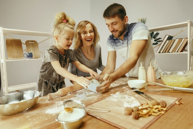 Niña linda y sus hermosos padres preparando la masa para el pastel en la cocina de casa