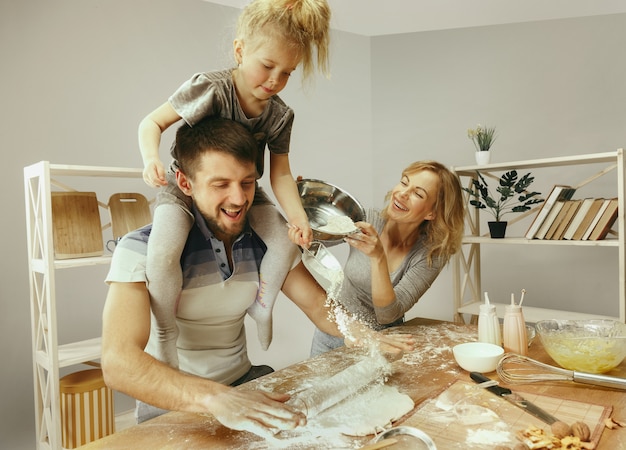 Niña linda y sus hermosos padres preparando la masa para el pastel en la cocina de casa