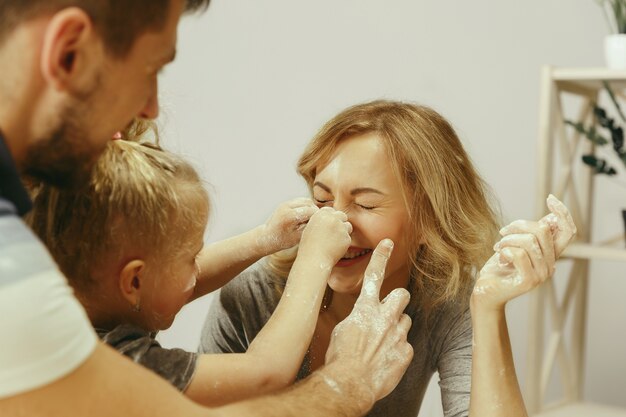 Niña linda y sus hermosos padres preparando la masa para el pastel en la cocina de casa