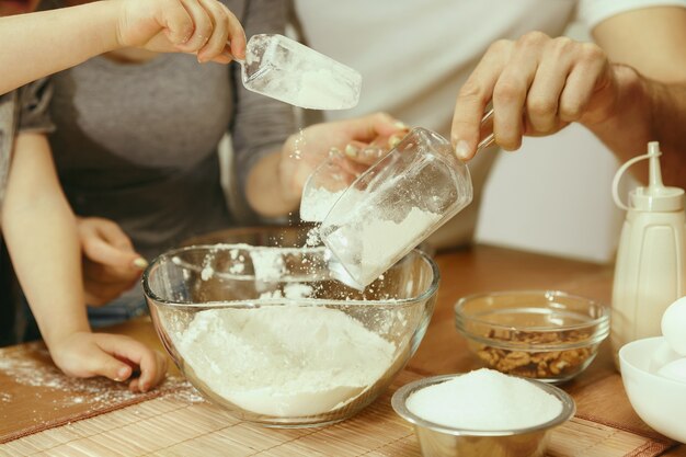 Niña linda y sus hermosos padres preparando la masa para el pastel en la cocina de casa.