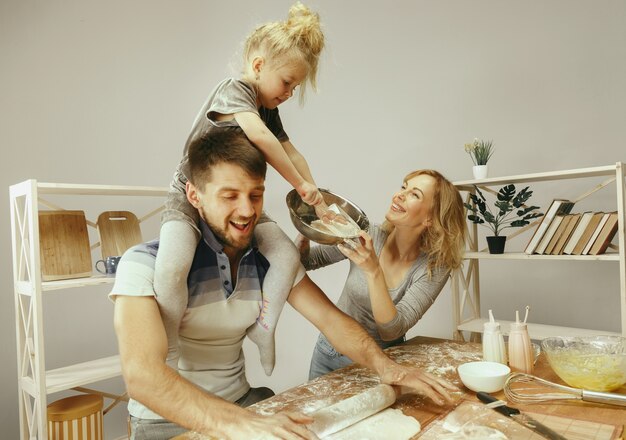 Niña linda y sus hermosos padres preparando la masa para el pastel en la cocina de casa.