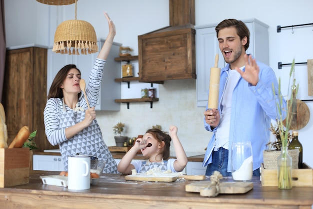 Niña linda y sus padres se divierten mientras cocinan juntos en la cocina en casa.