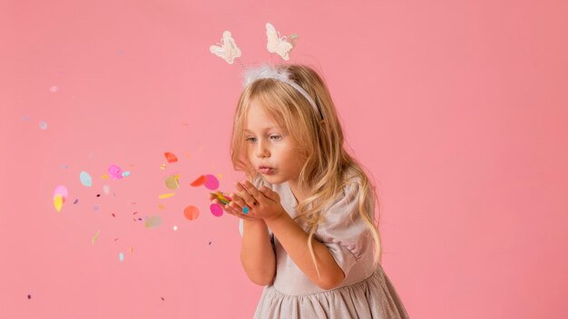 Niña linda en traje que sopla confeti