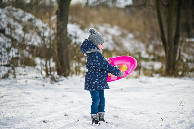 Niña linda con trineos de platillo al aire libre en día de invierno