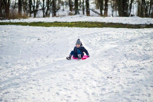 Niña linda con trineos de platillo al aire libre en día de invierno