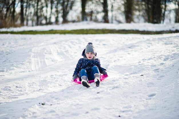 Niña linda con trineos de platillo al aire libre en día de invierno