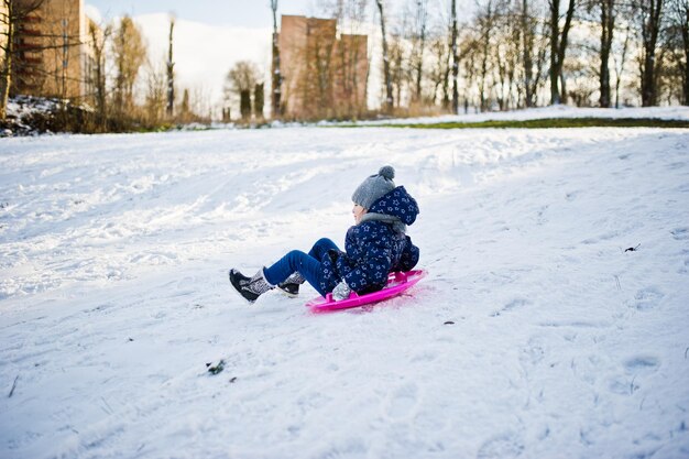 Niña linda con trineos de platillo al aire libre en día de invierno