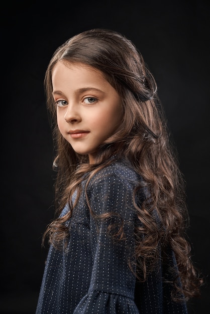 Foto gratuita niña linda en vestido gris sobre fondo negro.