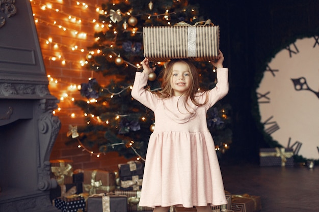 Niña con un lindo vestido cerca del árbol de navidad con presente