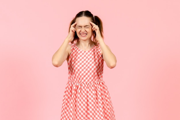 Foto gratuita niña en lindo vestido rosa que sufre de dolor de cabeza en rosa