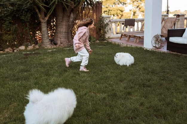 Niña y lindos cachorros blancos jugando al aire libre