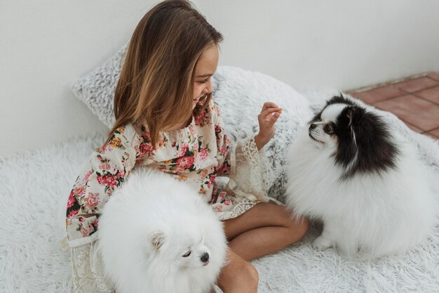 Niña y lindos cachorros blancos sentados en la cama
